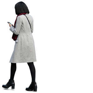 woman in a light grey coat walking and looking at her phone