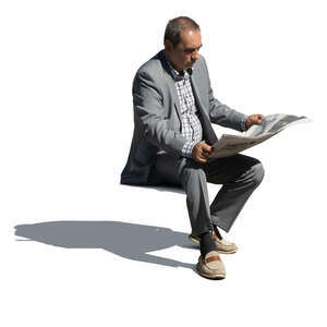 older man in a grey suit sitting and reading a newspaper