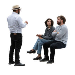 man standing and talking to two friends sitting
