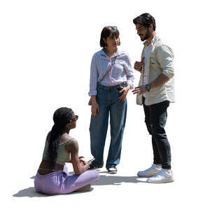 woman sitting on the ground and talking to two friends standing