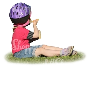 young girl with a helmet sitting on the grass and eating icecream
