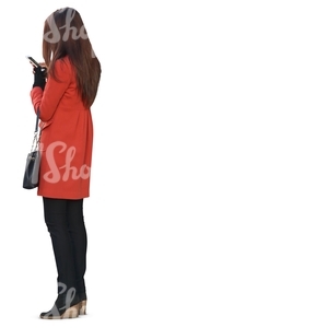 woman in a red coat standing and looking at her smartphone