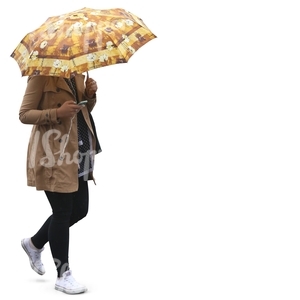 woman in a beige coat walking under an umbrella and listening to music