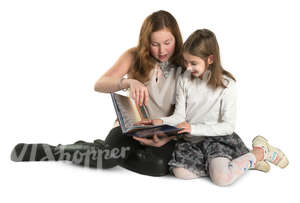 two girls sitting on the ground and reading a book