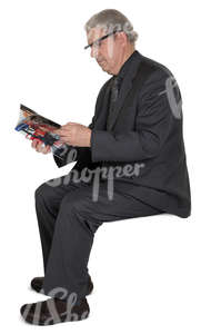 elderly man in a suit sitting and reading a newspaper