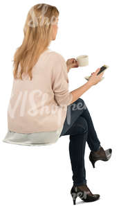 woman sitting and drinking coffee and looking at her phone