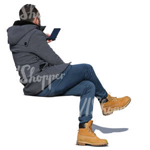 man in a grey autumn coat sitting and looking at his phone