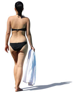 woman in a black bikini walking with a towel in her hand