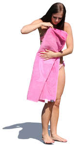 woman in a bikini standing and folding a pink towel