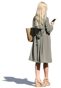 woman in a light trenchcoat standing and texting