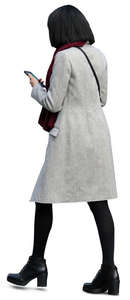 woman in a light grey coat walking and looking at her phone