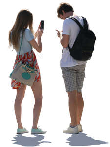 backlit young man and woman standing and checking their phones 