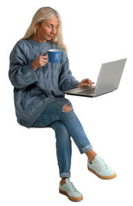 senior woman drinking coffee and looking at laptop