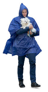 man wearing a blue hooded rain jacket walking and  carrying a small dog