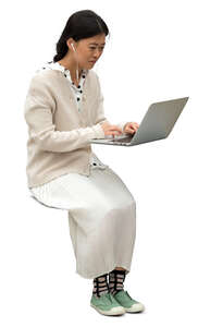 cut out asian woman sitting at a table and working with laptop