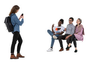 cut out young woman taking a picture of her three friend sitting on a bench