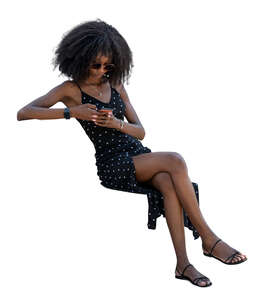 cut out black woman in a summer dress sitting and browsing her phone