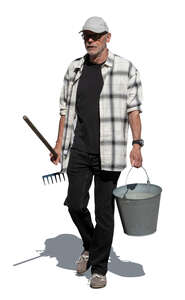 cut out older man walking in the garden carrying a bucket and a rake