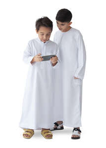 two cut out arab boys dressed in kandoras standing and watching tablet