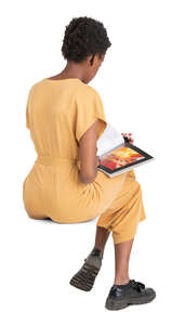 cut out woman in a yellow jumpsuit sitting and reading a magazine