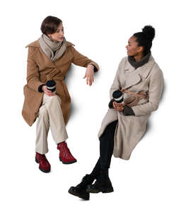 cut out top view of two women in overcoats sitting and talking