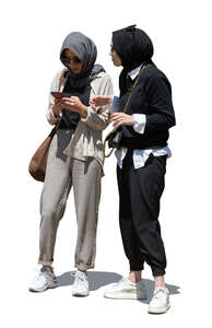 two cut out young muslim women standing and checking their phone