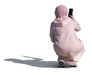 woman wearin g a pink abaya and hijab squatting and taking a picture