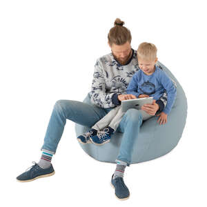 father and son sitting on a bean bag chair and watching tablet together