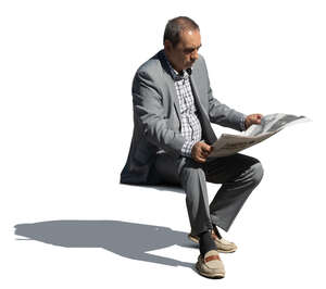 older man in a grey suit sitting and reading a newspaper