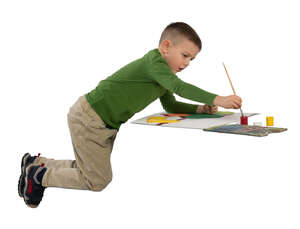 little boy sitting at a table and painting a picture 