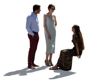 backlit woman sitting and talking to two friends standing in front of her