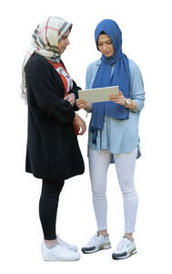 two muslim girls standing and looking at an ipad