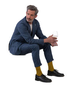 older man in a suit sitting and drinking wine
