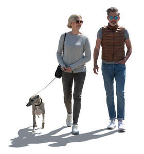 backlit man and woman walking a dog