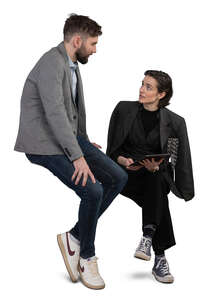 man sitting on a desk and talking to a woman sitting beside her