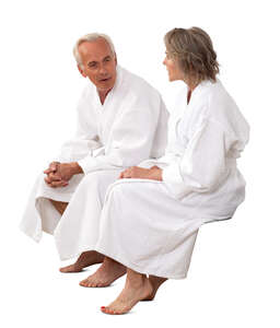 older man and woman in white bathrobes sitting and talking