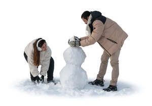 man and woman building a snowman in winter