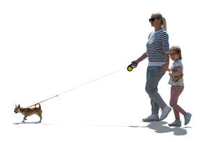 backlit mother and daughter walking hand in hand and walking a dog