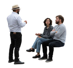 man standing and talking to two friends sitting