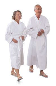 two older people wearing white bathrobes walking