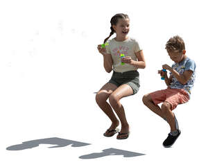 two backlit children sitting and blowing soap bubbles
