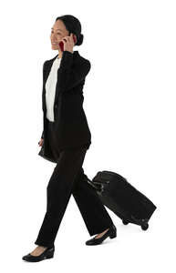asian woman in a suit with a travel suitcase walking and talking on the phone