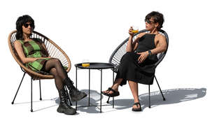 two women sitting in armchairs on a patio and talking