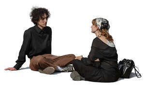 two young people sitting on the ground and talking