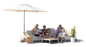 family sitting on a terrace on a sofa under a parasol