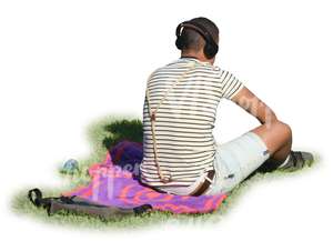 man with headphones sitting in a park on a blanket