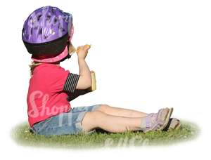 young girl with a helmet sitting on the grass and eating icecream