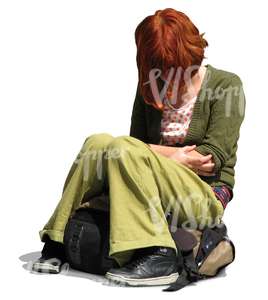 young woman with red hair and green clothes sitting on her backpack
