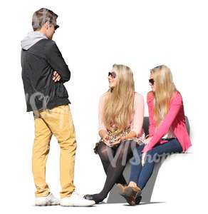 two women sitting and talking to a standing man