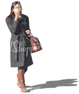black woman in a grey coat walking and drinking coffee